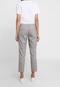 Jasnoszare spodnie w kratę o dopasowanym kroju, z kieszeniami z tyłu, prostymi nogawka i subtelnymi żółtymi akcentami. Stylizowane z białą koszulką.