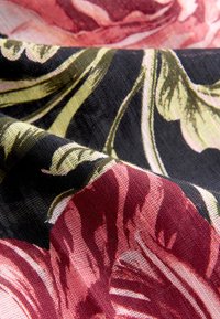 Textil med ett blommönster med stora röda och rosa rosor på svart bakgrund; slät textur, mjukt tyg, med gröna blad accenter.