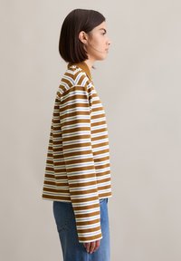 Gestreepte lange mouwen top in mosterdgeel en wit, met een ontspannen pasvorm en een kraag, gecombineerd met blauwe denim jeans.