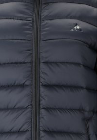 Marineblaue Steppjacke mit horizontalen Nähten, durchgehendem Reißverschluss und einem kleinen Logo in der oberen rechten Ecke. Glatte, glänzende Textur, isoliertes Design.