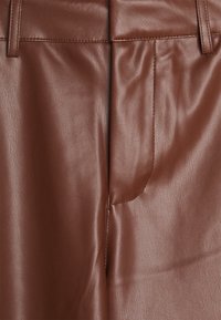 Brązowe spodnie z ekologicznej skóry o gładkiej fakturze, z przednią kieszonką i przeszyciami.