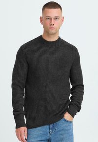Mørkegrå strikket sweater med rund hals, lange ærmer og ribbet struktur. Båret med blå denim jeans, der viser en afslappet pasform.
