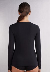 Schwarzes Langarmoberteil aus weichem Stoff, mit rundem Ausschnitt und tailliertem Design, kombiniert mit schwarzen Hosen.