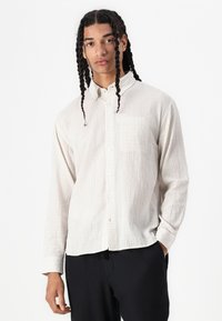 Chemise légère à manches longues avec un motif à carreaux, col boutonné, poche poitrine simple et coupe décontractée. Tissu doux et texturé.