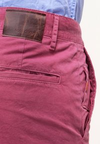Pink cotton shorts with a textured finish, featuring a brown leather patch labeled "BOSS ORANGE" and a side pocket.
