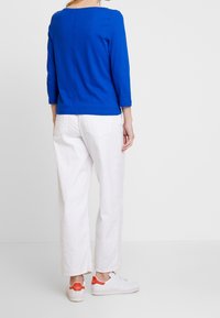 Royalblå, långärmad topp med rund hals, som passar bra med löst sittande vita byxor och vita sneakers med orange detaljer.