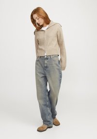 Beige ribbad zip-up tröja med bred krage, kombinerad med ljusblåt löst sittande jeans och ljusbruna ankelboots. Enkel, avslappnad outfit.