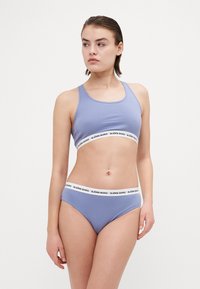 Világoslila sportmelltartó vastag fehér szalagon a "BJÖRN BORG" logóval; azonos színű, illeszkedő bikinitanga párosítva.