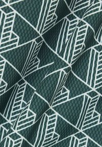 Donkergroen stof met wit geometrisch abstract stadsbeeldpatroon en subtiele geruite textuur, weergegeven met plooien en schaduwen.