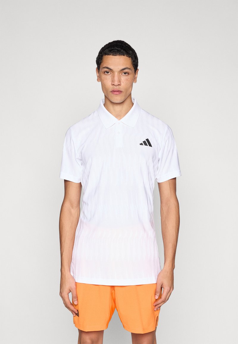 Biała koszulka polo z fakturowanym wzorem, krótkimi rękawami i kołnierzem; z czarnym logo adidas na lewej piersi. Połączona z pomarańczowymi szortami.