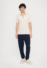 Bežna polo majica s kratkimi rokavi, zadrgo pri ovratniku in izvezenim logotipom. V kombinaciji z modrimi trenirkami in off-white tenisicami za sproščen videz.
