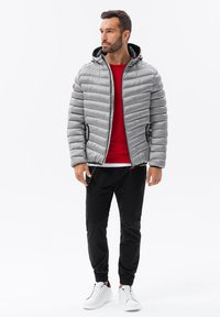 Grå puffjacka med horisontell söm och huva, kombinerad med en röd tröja med rund hals, svarta joggarbyxor och vita sneakers.