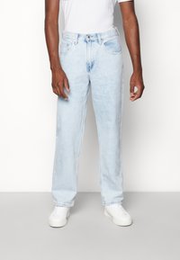 Ljust blå denimjeans med rak bendesign, femficksstil och kontrasterande sömmar, tillsammans med vita sneakers.