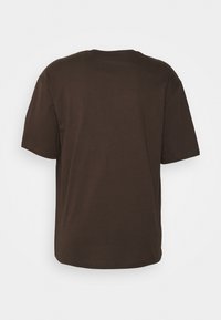 T-shirt marrone a maniche corte con scollo rotondo, realizzato in cotone, caratterizzato da una texture liscia e un design con vestibilità rilassata.