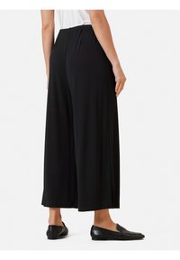 Zwarte wijde broek met een elastische tailleband, gladde stof en enkel-lengte ontwerp, gecombineerd met zwarte instapschoenen.