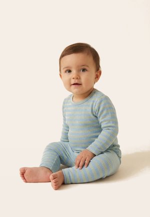 Toddler sidder på gulvet iført blå og grå stribet langærmet top og matchende bukser, kigger frem med et neutralt udtryk.