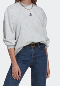 Grå sweatshirt med ribbad krage och sänkta axlar, med en liten svart Adidas-logga. Matchad med högmidjade blå jeans och ett svart bälte.