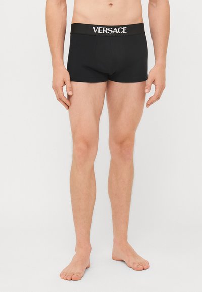 Schwarze Baumwollboxershorts mit einem elastischen Bund, der das Versace-Logo in Weiß zeigt. Das Design ist körperbetont und hat eine mittellange Länge.