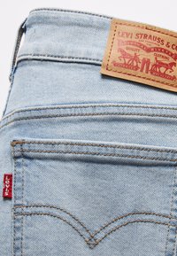 Hellblaue Denim-Jeans mit einem Lederpatch auf der Rückseite, versehen mit gesteppten Details und einem kleinen roten Levi's-Tab am Taschenrand.