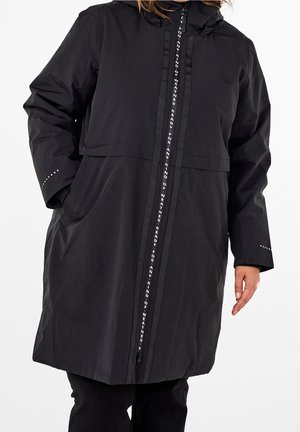 Abrigo largo de lluvia negro con capucha, cierre con cremallera que lleva texto blanco "Preparado para cualquier tipo de clima", manos de una persona parcialmente visibles.