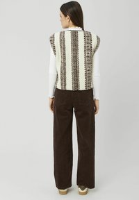 Gilet en maille polaire avec un motif crème et marron, associé à un pantalon large en velours côtelé marron et des baskets beige.