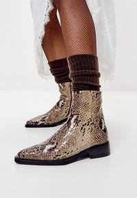 Botas de tobillo con estampado de serpiente y puntera afilada, hechas de material sintético brillante, con un tacón bajo y superficie texturizada.