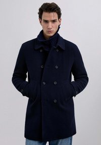 Marineblå uldblandingsfrakke med klapkrave, dobbeltknaplukning, sidelommer og ribstrikket kravedetalje.