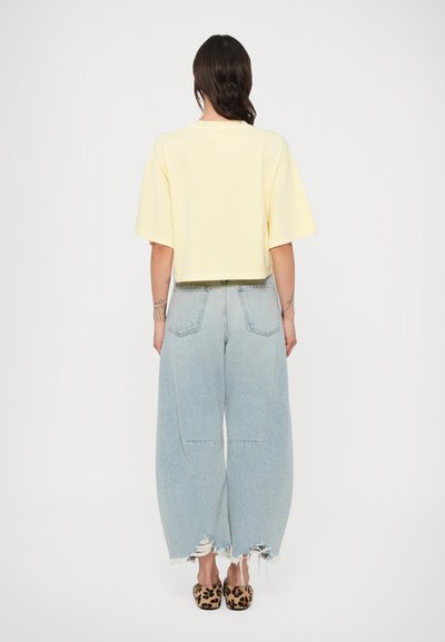 T-shirt jaune court à manches larges associé à un jean bleu clair, taille haute, jambes larges avec bords effilochés et poches arrière.