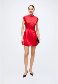Mini-robe en satin rouge avec un col montant et des manches courtes, texture lisse, silhouette ajustée, assortie à des talons noirs et une pochette.
