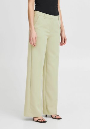 Pantalons larges vert clair avec une texture lisse, poches avant et taille ajustée. Associés à des sandales noires à lanières.
