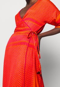 Wrapklänning i ljus orange och rosa, med geometriska mönster, djup V-ringning, korta ärmar och detalj med knyt i midjan.