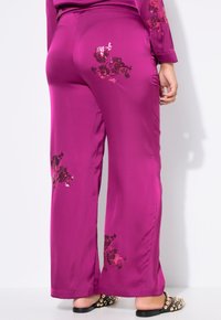 Magenta satijnen broek met florale borduursels aan de zijkanten, wijde pijpen en een platte tailleband.