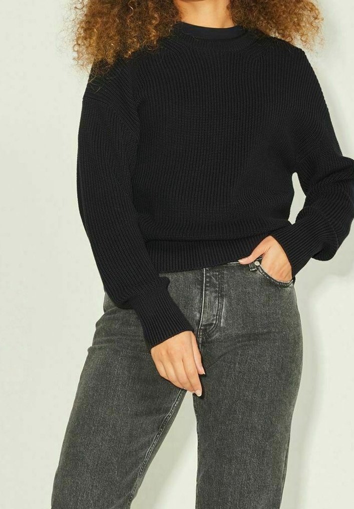 Maglione nero lavorato a maglia con texture a costine, scollo tondo e maniche lunghe, abbinato a jeans grigi scuri a vita alta.