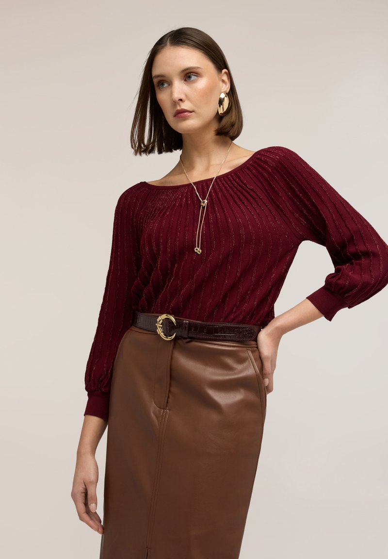 Bordeaux geribbelde gebreide trui met een off-shoulder halslijn, gecombineerd met een bruine leren kokerrok en een gestructureerde bruine riem met een gouden gesp.
