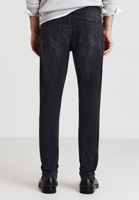 Jeans in denim nero con una vestibilità slim, dotati di cinque tasche, cuciture sottili e una texture leggermente scolorita. Indossati con scarpe nere.