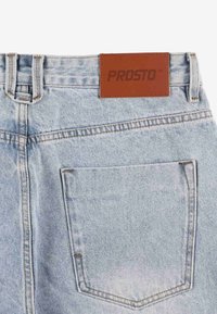 Jasnoniebieskie dżinsy z denimu z brązową skórzaną łatą z napisem "PROSTO." Tylna kieszeń z widocznym przeszyciem i teksturowanym detalem tkaniny.