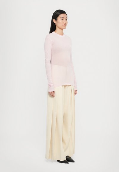 Top roz deschis cu mânecă lungă, cu un design ajustat, textură stratificată, asociat cu pantaloni largi crem și balerini negri cu vârful ascuțit.