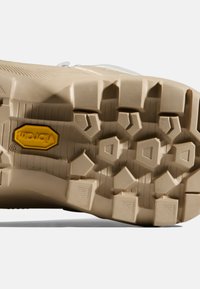 Beżowa podeszwa butów hikingowych z agresywnym wzorem trakcji, z wielokierunkowymi wypustkami i żółtym logo Vibram, gwarantującym trwałość.
