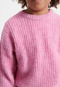 Ružový pletený sveter s rebrovanou textúrou a okrúhlym výstrihom, ktorý má mäkké vlákna a voľný strih, ideálny na bežné nosenie.