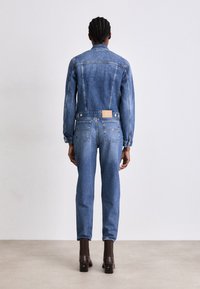 Jeansjacka i en urblekt blå färg med knapprad, tillsammans med matchande jeans som har en lätt avsmalning och bakfickor.