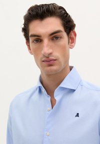 Camicia azzurra a quadretti con colletto button-down, caratterizzata da un piccolo logo di teschio navy sul petto e bottoni beige.