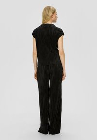 Zwart geplooid twee-delig outfit met een korte mouwen top en wijde pijpen, beiden met een geribbelde structuur en vloeiende silhouette.