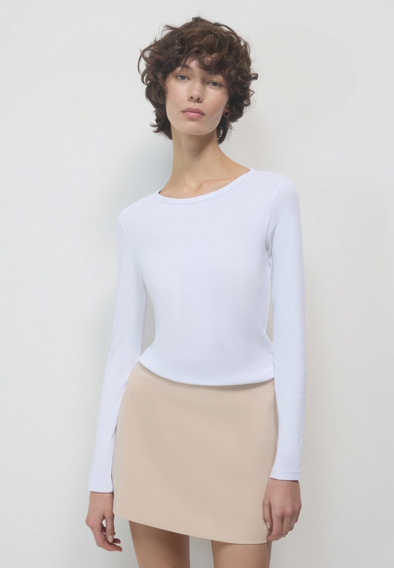 Top bianco a maniche lunghe con collo rotondo, abbinato a una mini gonna beige. Texture liscia, vestibilità slim e design minimalista. Nessun motivo o accento.