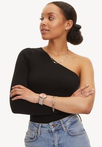 Sort ribbet én-skulder top parret med højtaljede denim jeans. Accessories inkluderer lagdelte sølv halskæder og et sølv ur med en pink urskive.