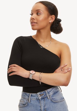Sort ribbet én-skulder top parret med højtaljede denim jeans. Accessories inkluderer lagdelte sølv halskæder og et sølv ur med en pink urskive.