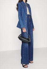 Chaqueta de mezclilla con lavado claro, botones grandes y un corte ajustado; pantalones de mezclilla oscuros de pierna ancha combinados con un bolso negro y sandalias planas.