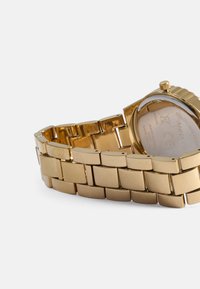 Montre-bracelet en métal doré avec un bracelet à maillons rectangulaires, un cadran texturé et un visage rond. Présente une couronne sur le côté et un dos en acier inoxydable.