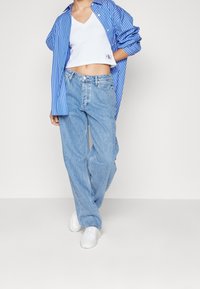 Sini-valkoinen raidoitettu ylipitkä paita valkoisen lyhyen v-kaula-aukon tanktopin päällä, yhdistettynä vaaleansinisiin leveälahkeisiin farkkuihin ja valkoisiin tennareihin.