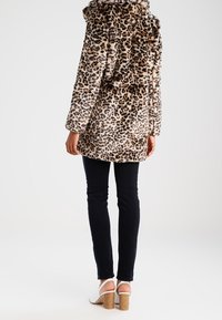 Leopardmönstrad faux fur-kappa med huva, långa ärmar och avslappnad passform, kombinerad med mörka jeans och beige blockklack-sandaler.