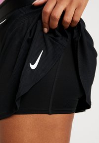 Nike mustat urheiluhousut, joissa on ribbikuviointi ja valkoinen logo. Kangas näyttää kevyeltä ja siinä on hieman kiiltoa. Ominaisuuksiin kuuluu hengittävä muotoilu.